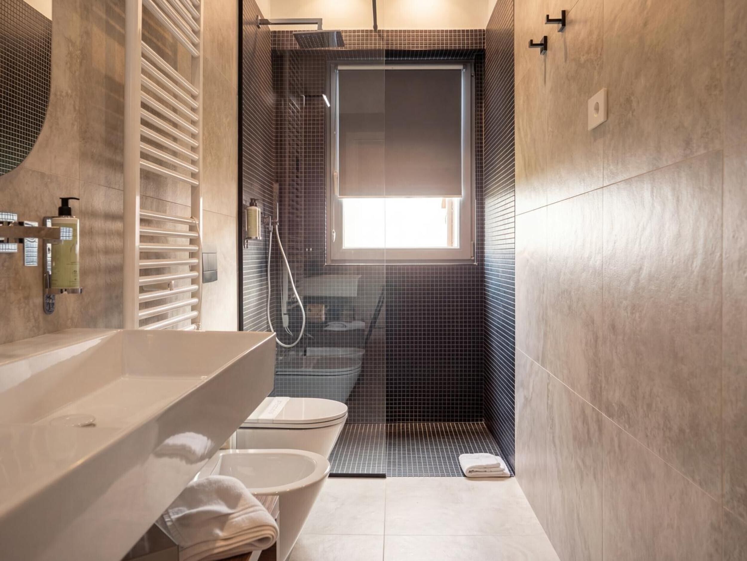 Un bagno moderno con vasca, WC e zona doccia, dotato di una grande finestra e un porta asciugamani.