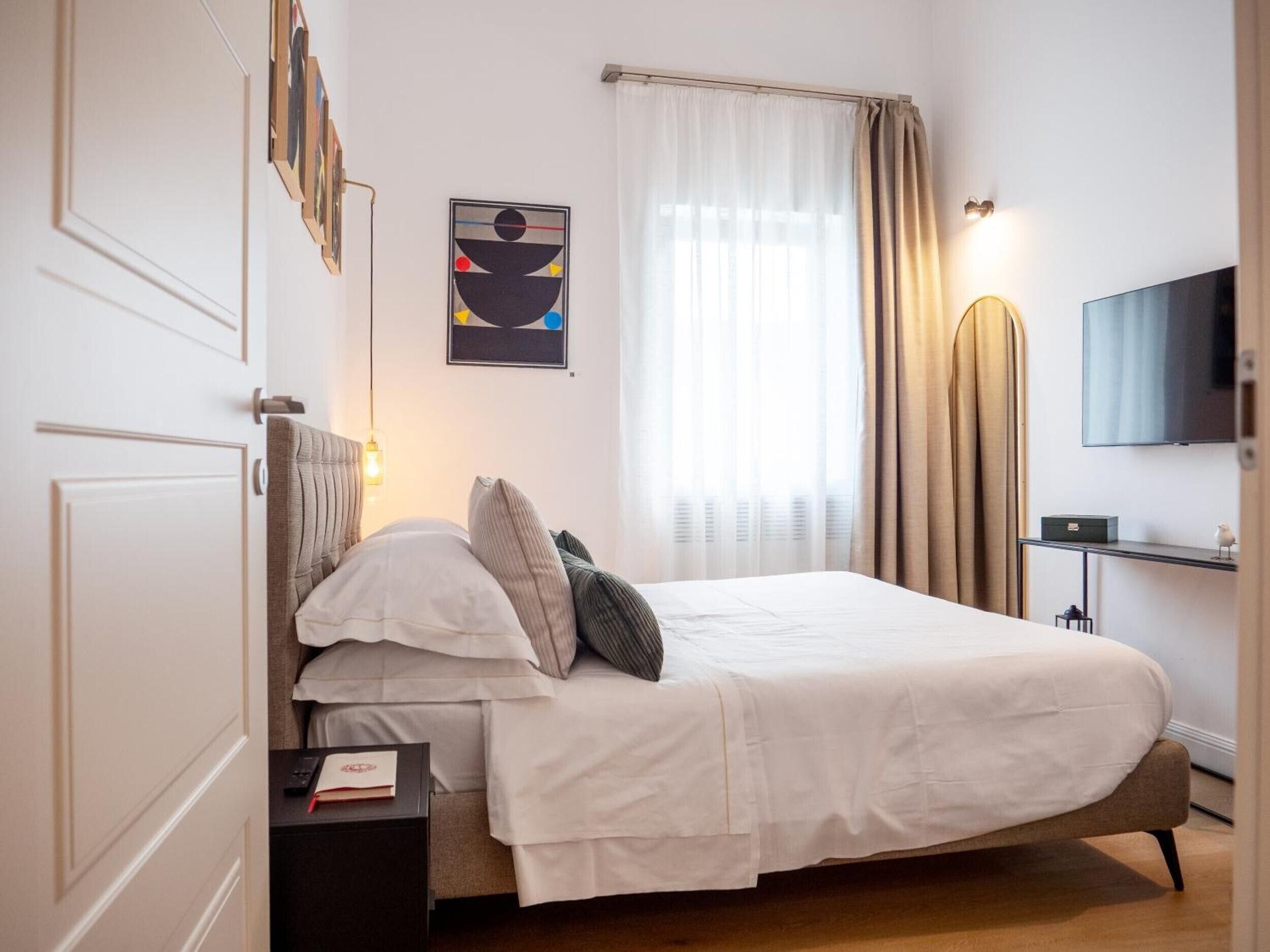 Une chambre à coucher bien rangée, avec un lit, des tables de chevet, un téléviseur et un tableau accroché au mur.