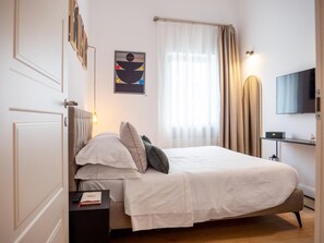 A neatly arranged bedroom with a bed, bedside tables, a television, and a painting on the wall.