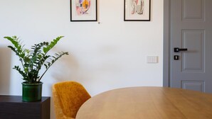 Una habitación con una mesa de madera, una planta en maceta verde, una silla amarilla y dos cuadros en la pared.