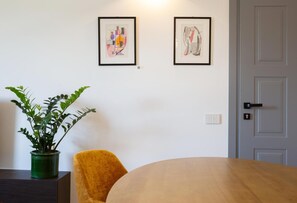 Una habitación con una mesa de madera, una planta en maceta verde, una silla amarilla y dos cuadros en la pared.