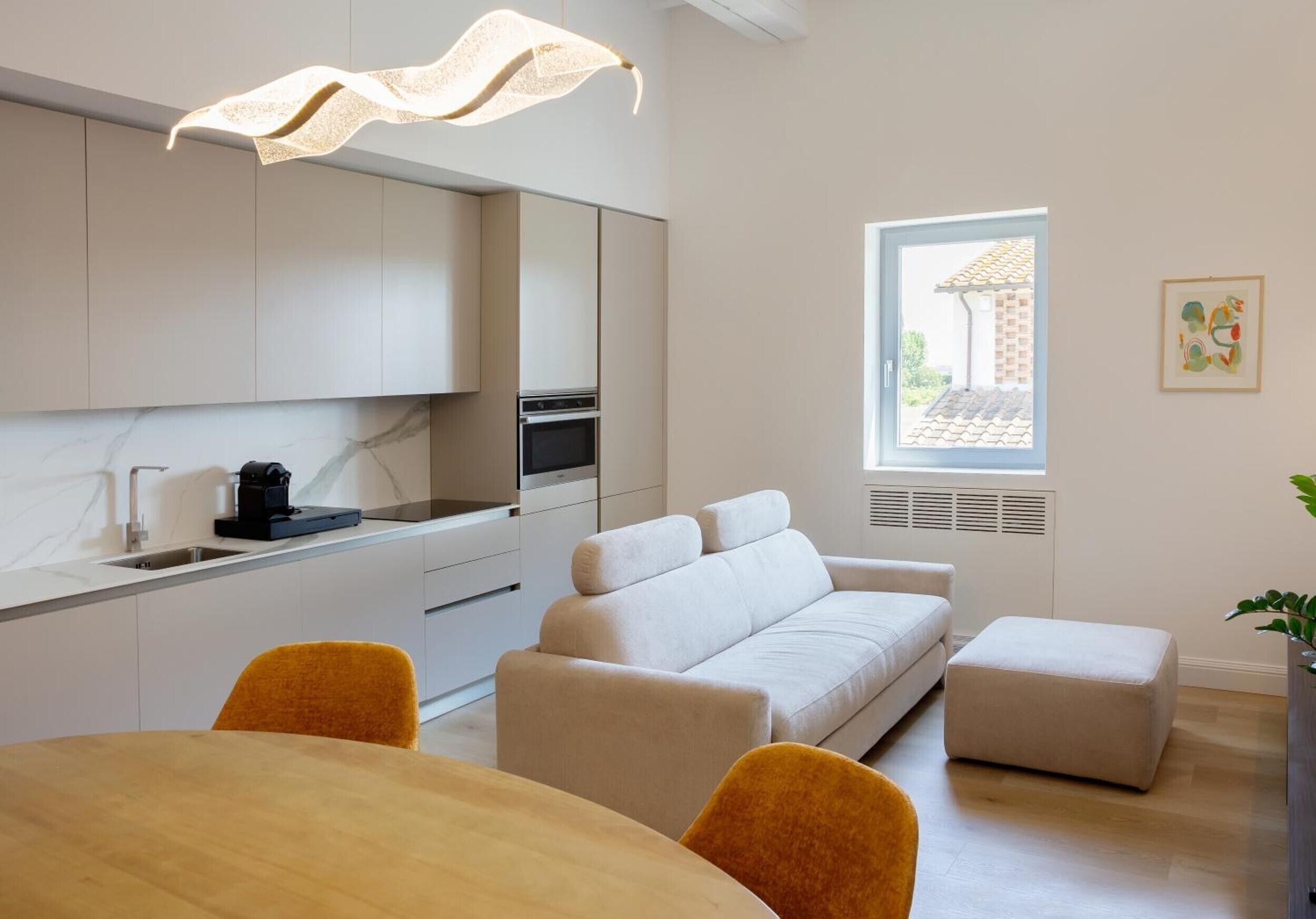 Une cuisine moderne dotée d’un four encastré, une table à manger avec des chaises et un canapé dans un espace de vie agrémenté d’une fenêtre.