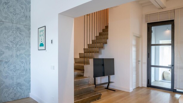 Un escalier au design moderne, un téléviseur à écran plat sur le palier et une porte dotée d’un panneau en verre.