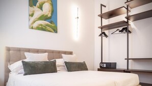 Un lit bien fait, avec une tête de lit, une table de chevet sur laquelle se trouve une télécommande et un porte-manteau fixé au mur.