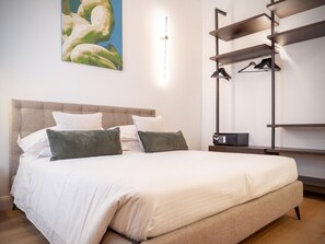 A neatly made bed with a headboard, a bedside table with a remote control, and a wall-mounted coat rack.