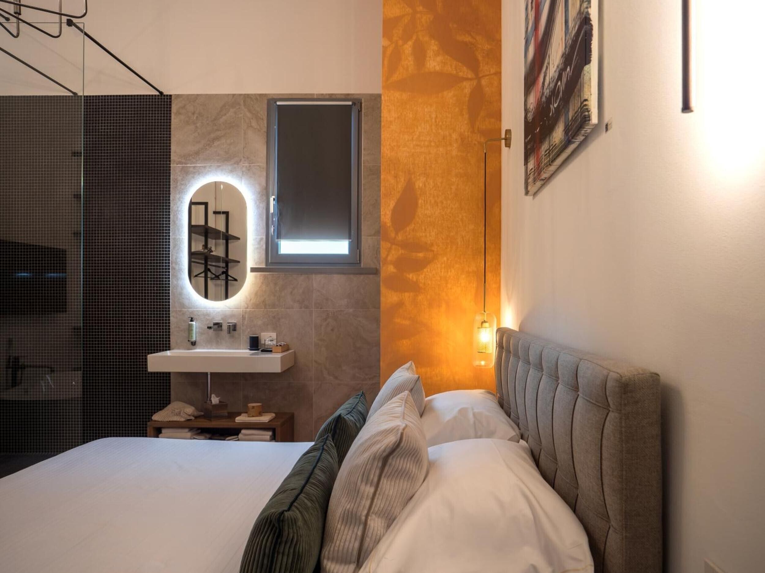 Ein modernes Schlafzimmer mit Bett, Nachttisch, Spiegel, Wandleuchte und einer Duschkabine.