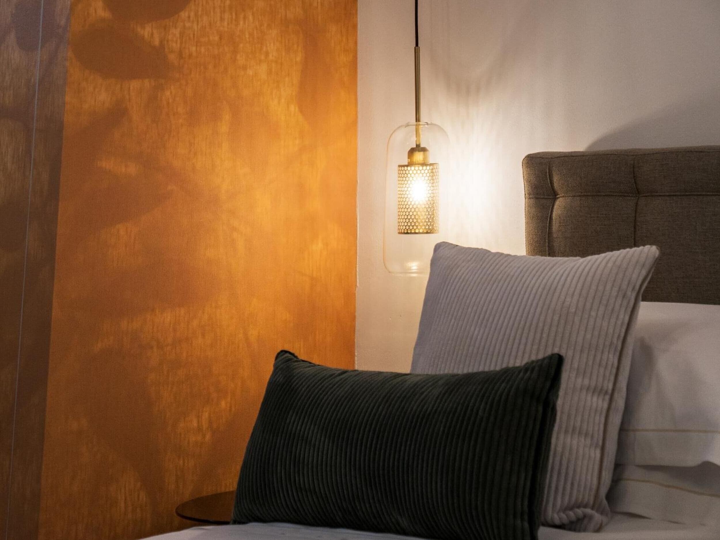 Ein Schlafzimmer mit einem Bett, Kissen, einem Nachttisch und einer Wandlampe.