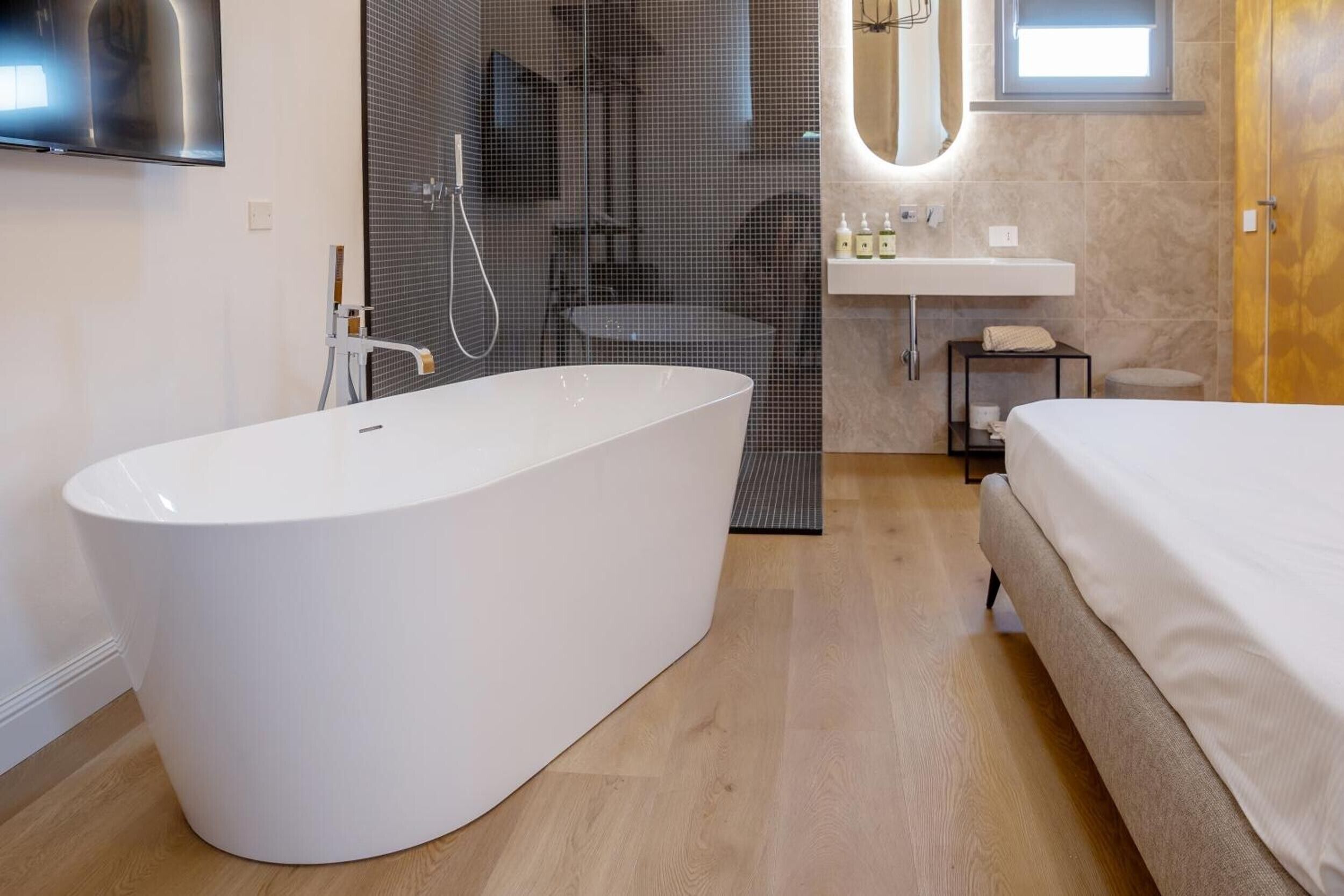 A modern bathroom with a freestanding bathtub, a shower enclosure, a vanity with a sink, and a bed.