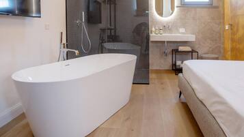 A modern bathroom with a freestanding bathtub, a shower enclosure, a vanity with a sink, and a bed.