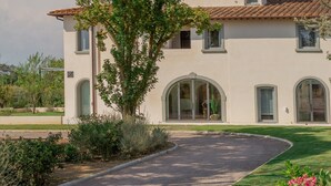 Une maison à deux étages, dotée d’une allée incurvée, entourée d’un jardin bien entretenu et de plantes en fleurs.