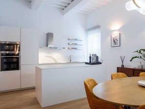 A modern kitchen with built-in appliances, a central island, and a dining area with a round table and chairs.