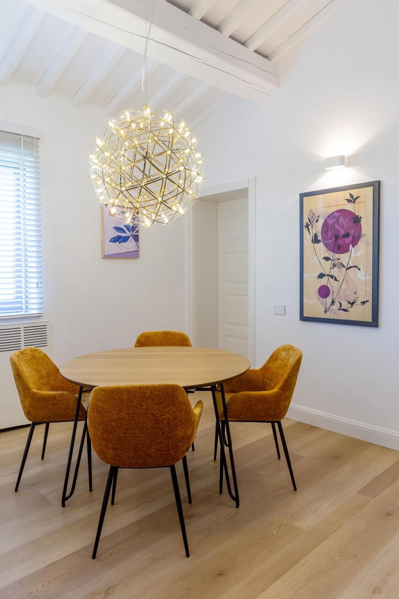 Un coin repas comprenant une table ronde, quatre chaises, un lustre aux motifs géométriques et deux œuvres d’art murales.