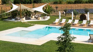 Un área de piscina con sillones de descanso y una zona de estar con sombra.