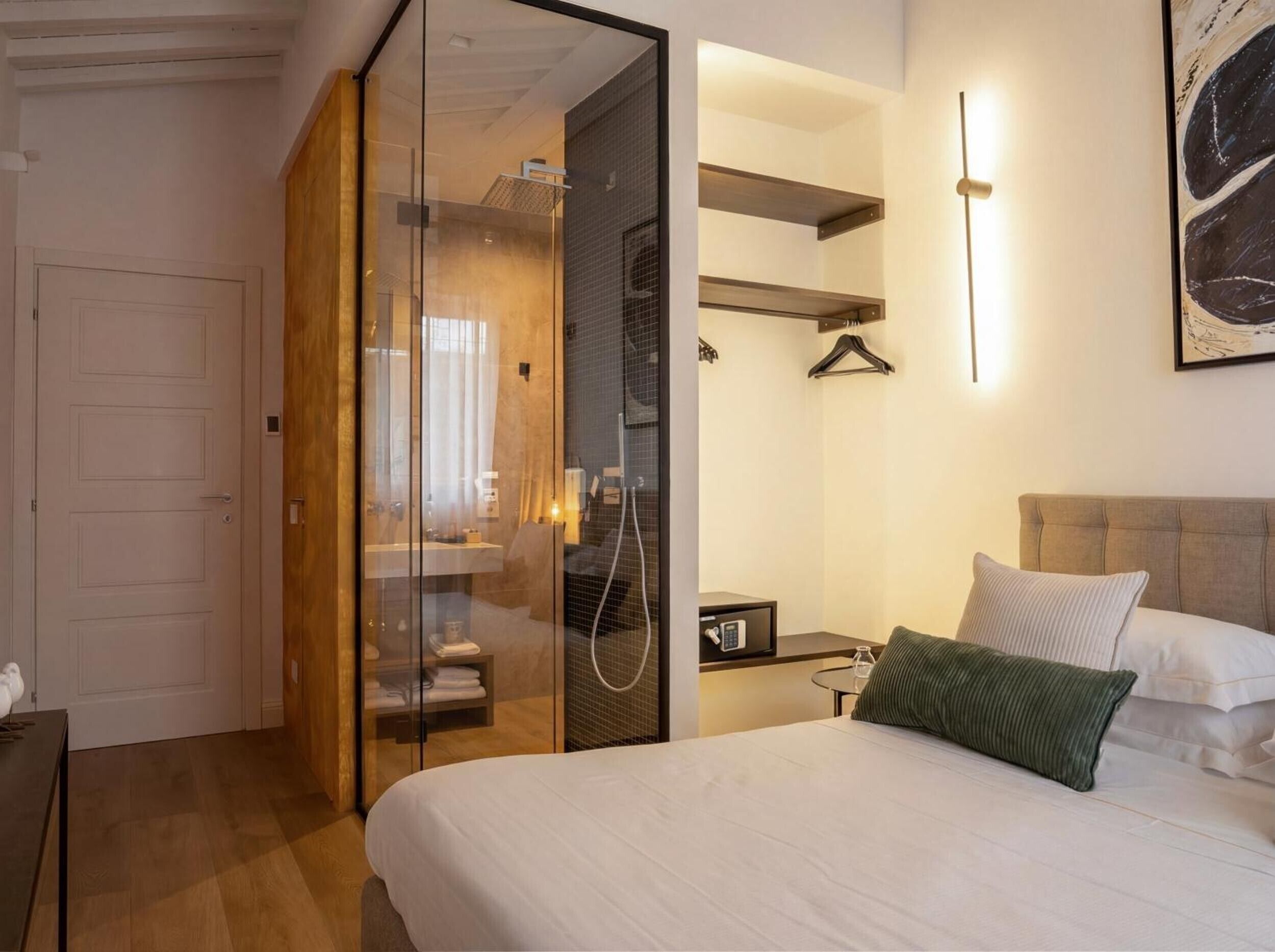 Una camera d'albergo con un letto, un comodino, uno specchio, una lampada a sospensione, un armadio e uno spazio doccia.