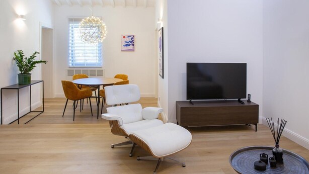 Una sala de estar moderna con un televisor de pantalla plana, un comedor con una mesa redonda y sillas, y una zona de estar con un sofá.