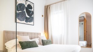 Habitación de hotel con una cama grande, una mesita de noche, un espejo y un cuadro en la pared.