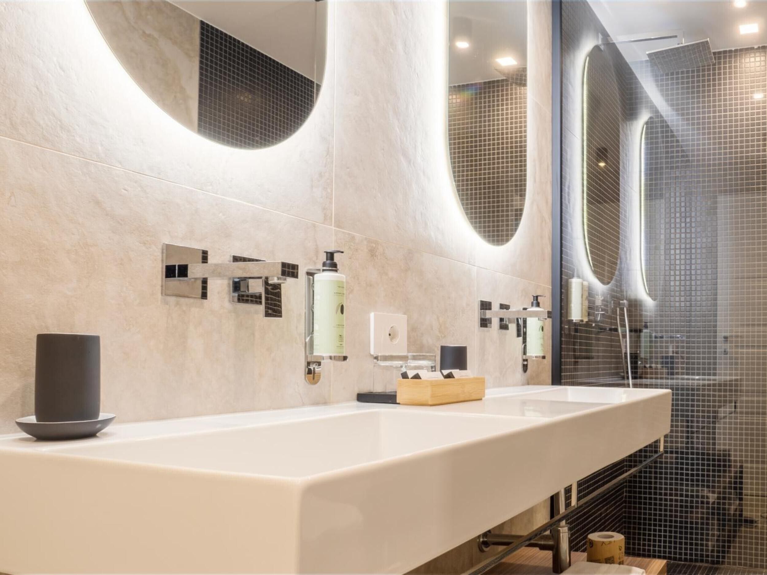 Un baño moderno con un espejo grande, un lavamanos blanco y una zona de ducha.