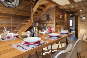 Comedor de madera con una larga mesa dispuesta para una comida, incluyendo botellas de vino y copas.