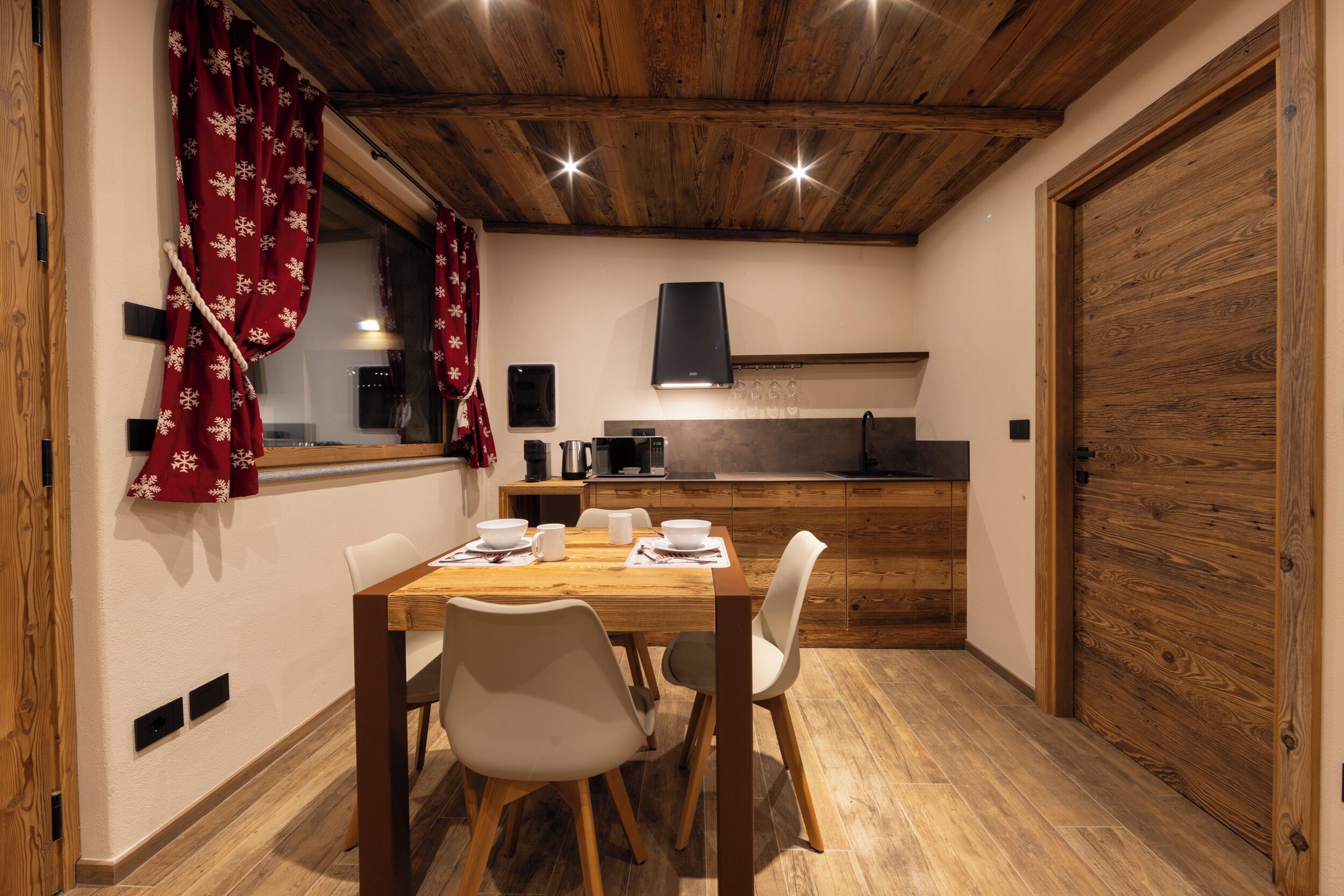 Ein Essbereich mit Holztisch und -stühlen, im Hintergrund eine Küche und eine Holztür.