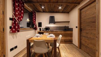 Ein Essbereich mit Holztisch und -stühlen, im Hintergrund eine Küche und eine Holztür.