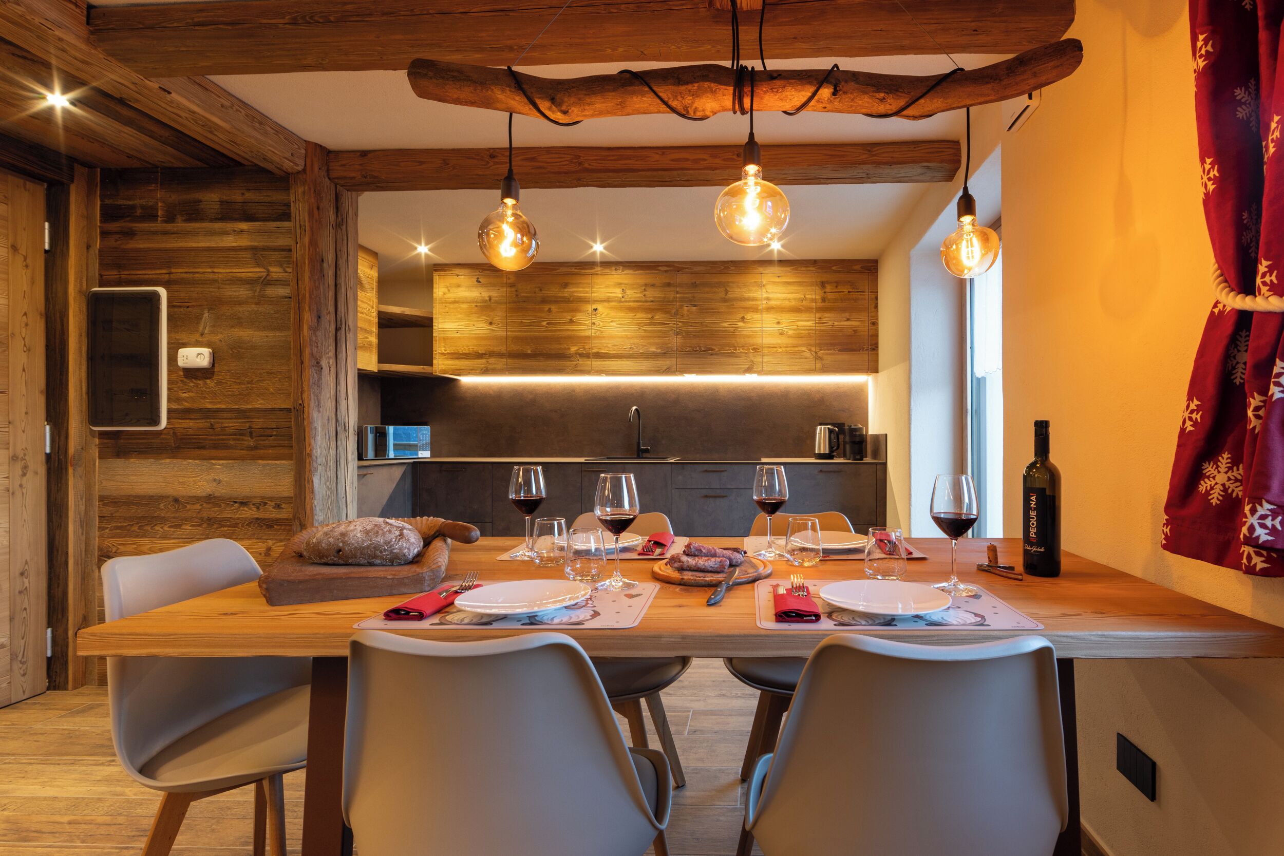 Un'area pranzo con un tavolo di legno apparecchiato per un pasto, una bottiglia di vino e un soffitto dal design rustico.