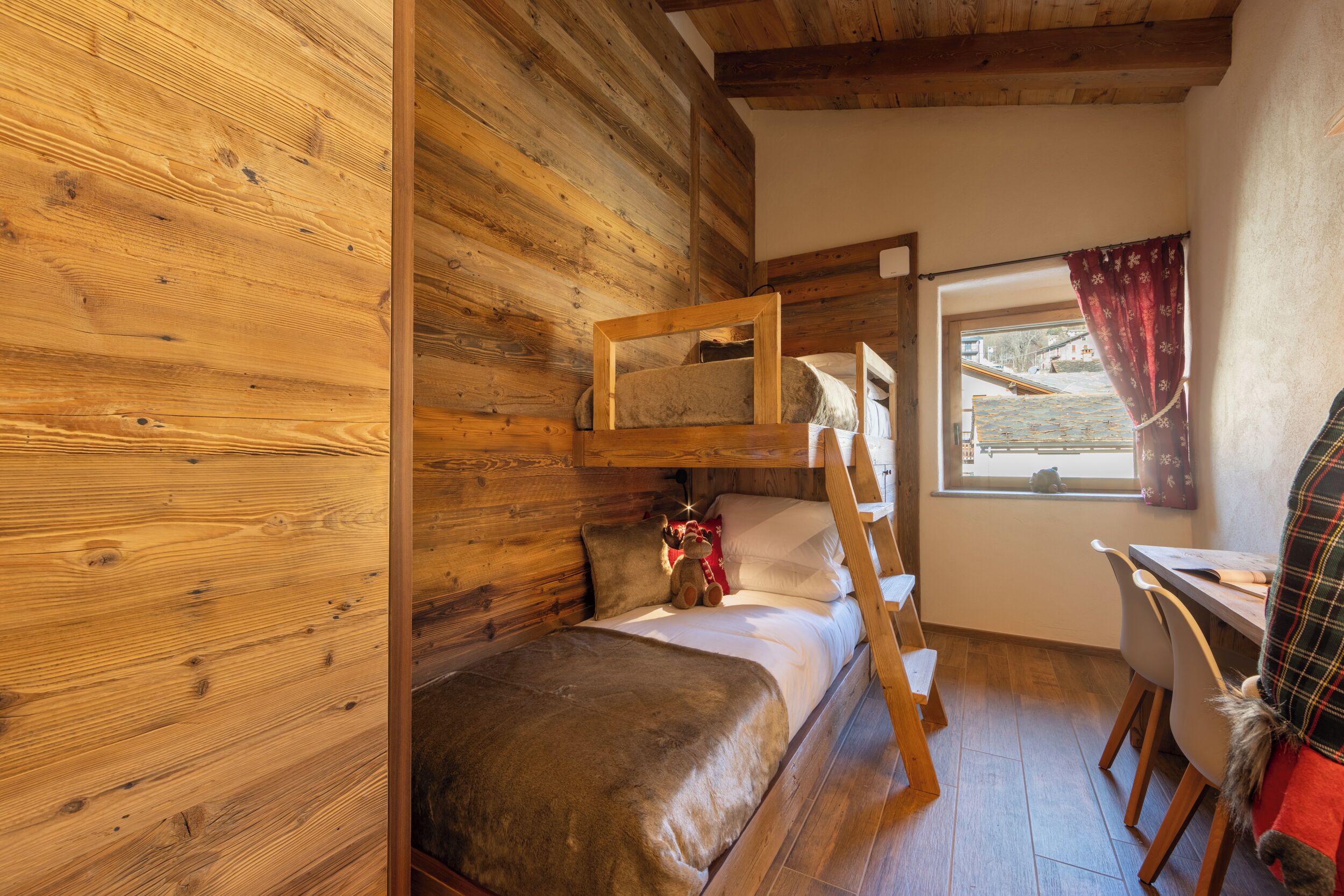 L'interno di una baita in legno con un letto a castello, una scrivania e una finestra con tende.