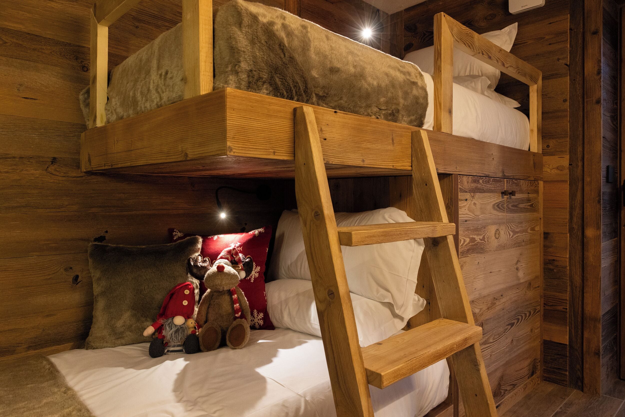 Ein Stockbett mit einer Leiter, ein Kuscheltier und ein Kissen an einer Holzwand.