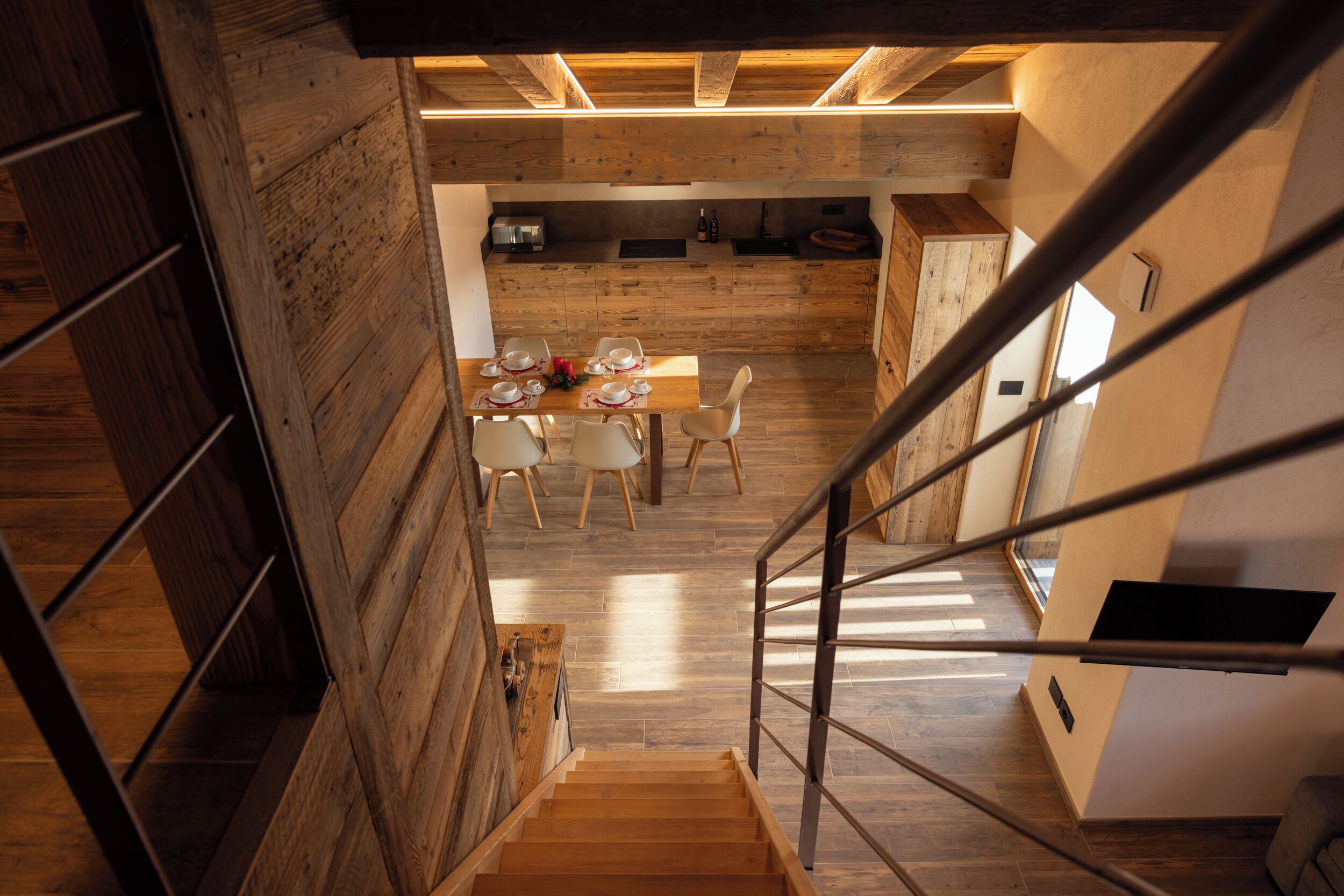 Ein modernes Interieur mit einer Holztreppe, einem Essbereich mit Tisch für vier Personen und einer Küche im Hintergrund.