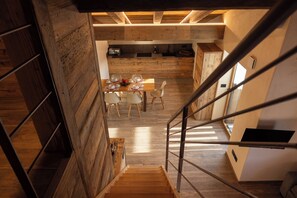 A modern interior with a wooden staircase, a dining area with a table set for four, and a kitchen in the background. - Les reves des Montagnards (Torgnon)