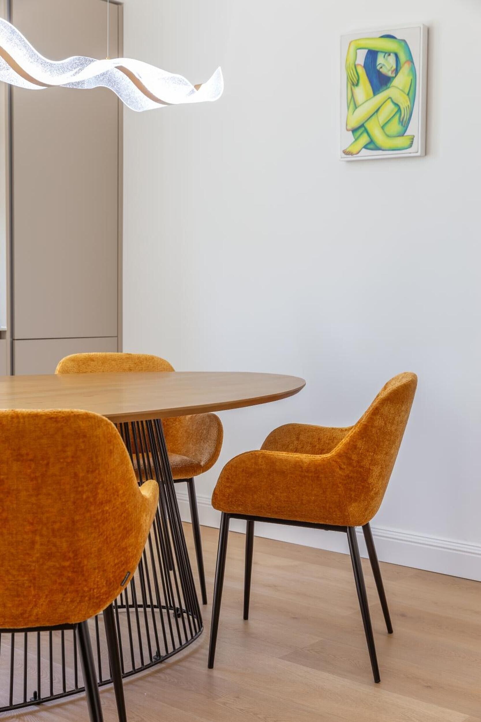 A dining area with a round table and four chairs, a hanging light fixture, and a piece of abstract art on the wall.