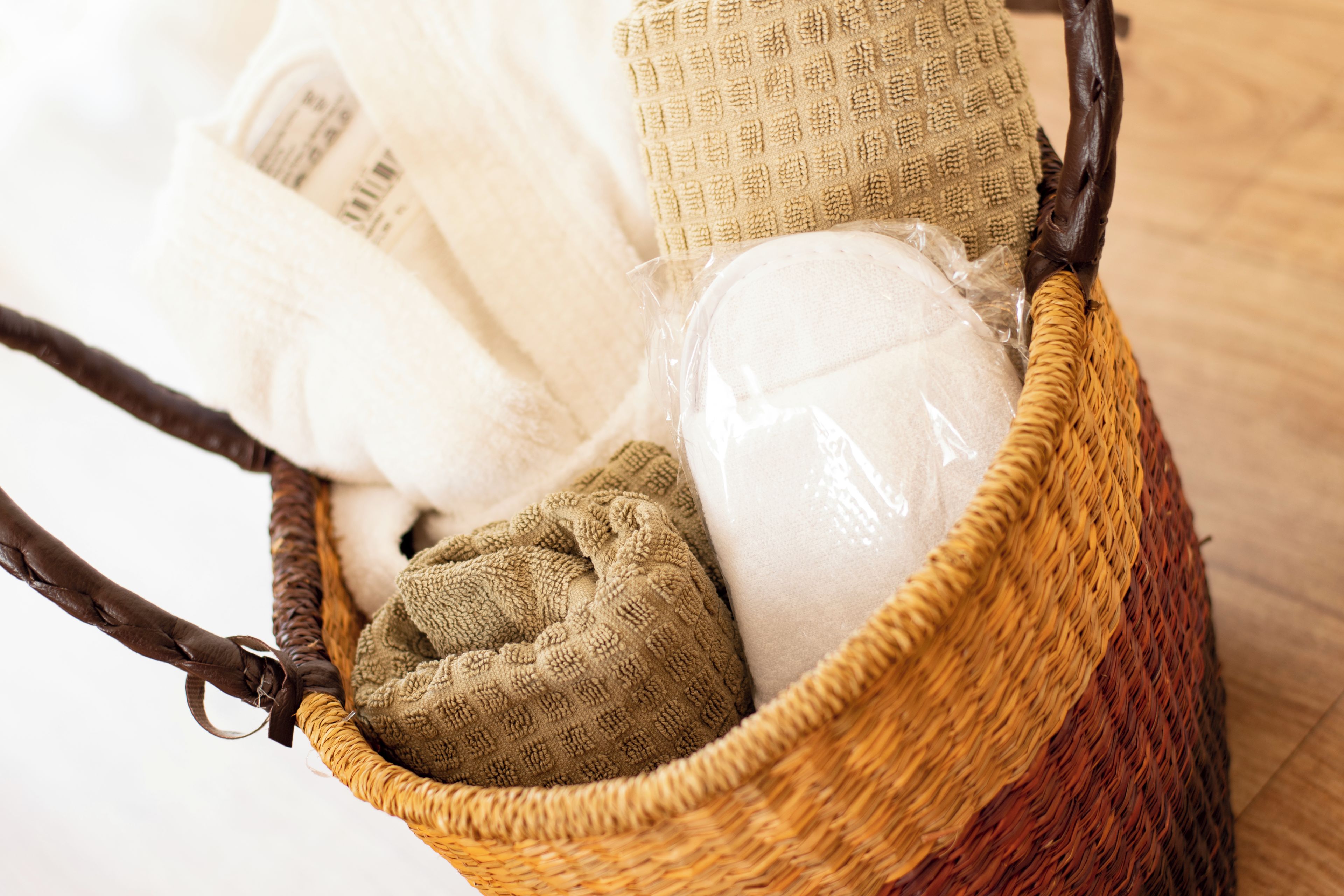 Una cesta de mimbre con varias texturas, incluyendo una almohada blanca, una toalla marrón y un tejido color beige.