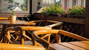 Et udendørs opholdsområde med træborde og stole, et skilt for 'Brauers 800°C Restaurant' og udsigt over byen i baggrunden.