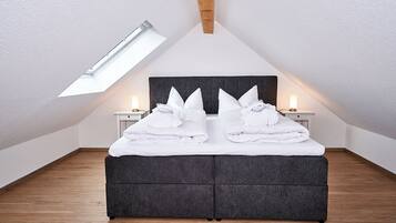 Un dormitorio con techo inclinado, tragaluz, cama con almohadas y lámparas de noche.