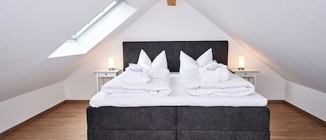 Un dormitorio con techo inclinado, tragaluz, cama con almohadas y lámparas de noche.