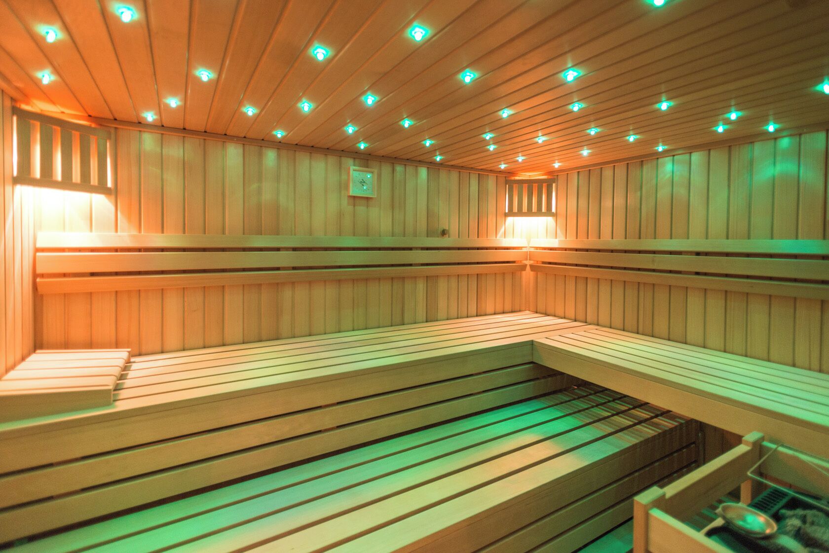 A sauna with wooden benches and a sloped floor, equipped with ceiling lights.