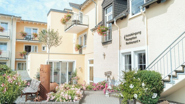 En hotelindgang med receptionsdisk, trappe og blomsterarrangementer.