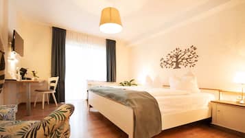 Habitación de hotel con cama, mesita de noche, lámpara, escritorio, silla y una obra de arte en la pared con motivos de árbol decorativo.