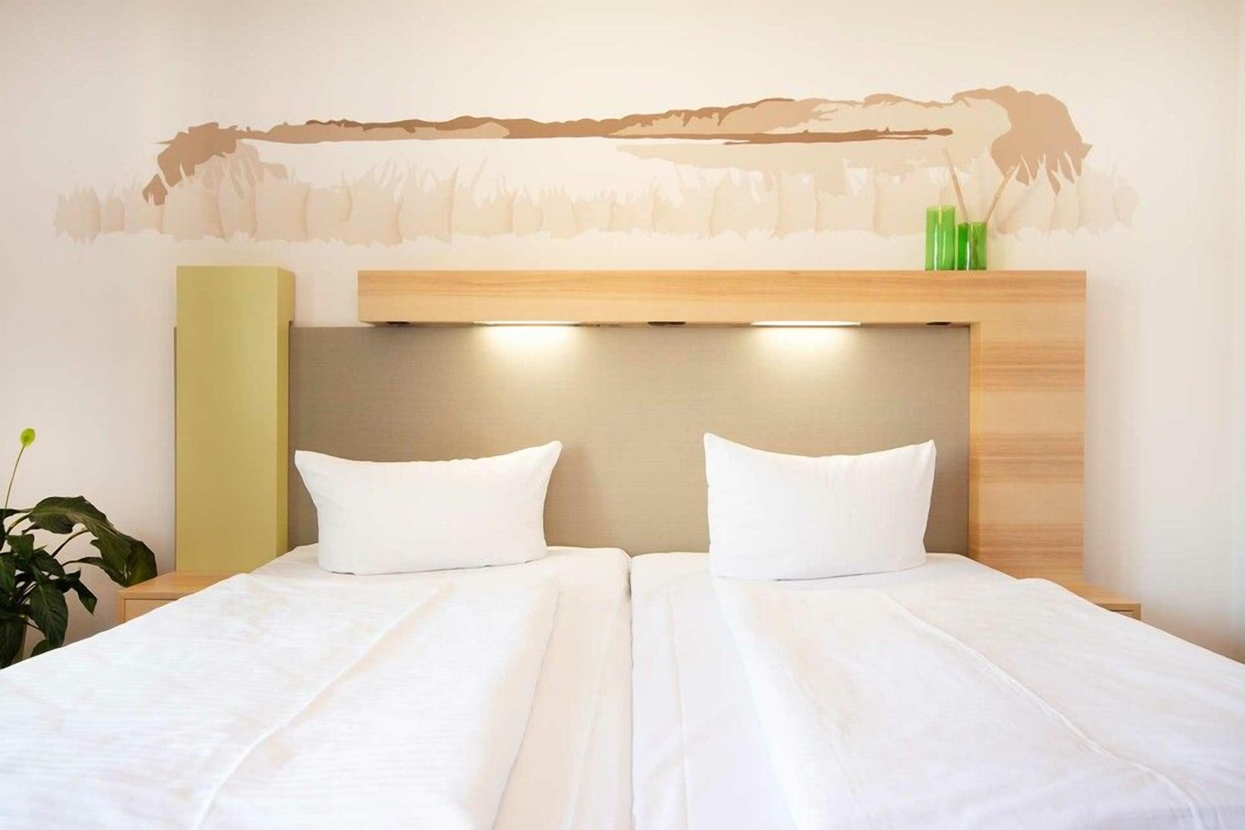 A double bed with white bedding, a wooden headboard, and a wall-mounted shelf with green vases.