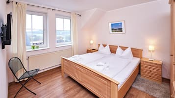 Ein Hotelzimmer mit einem hölzernen Bett, zwei Nachttischen, einem Sessel, einer Heizung und einem an der Wand befestigten Fernseher.