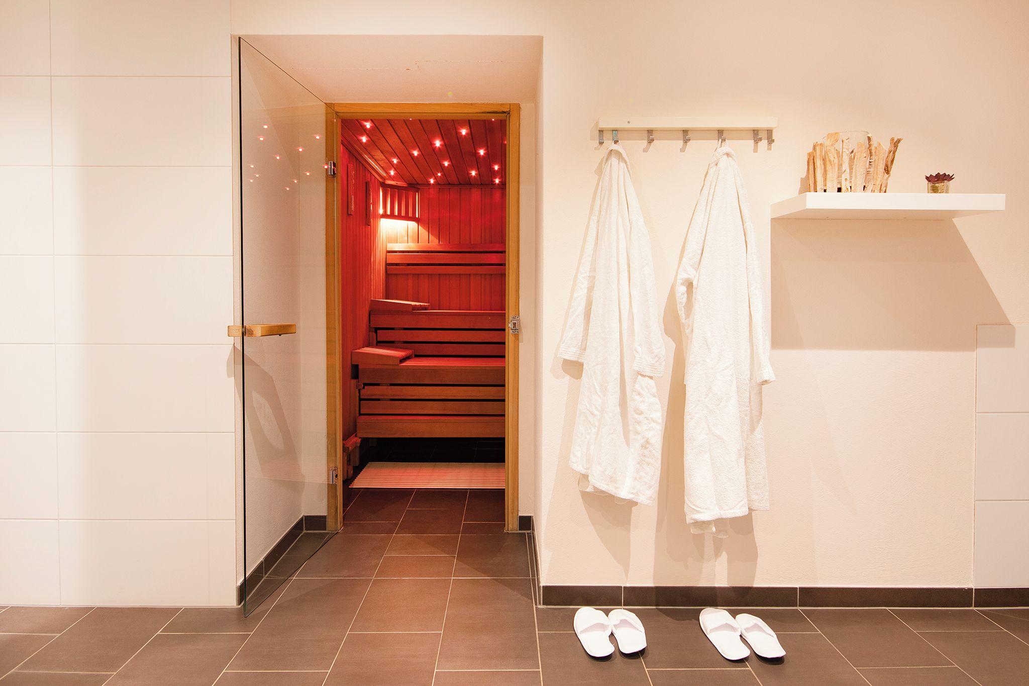 Un baño de hotel con zona de ducha, un perchero con toallas y un par de pantuflas en el suelo.
