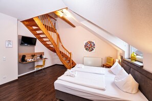 A hotel room with a wooden staircase, a bed, a desk, and a television. - Brauers Landarthotel (Daun)