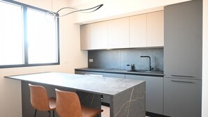 Cozinha moderna com ilha de mármore, dois bancos altos e uma janela grande.