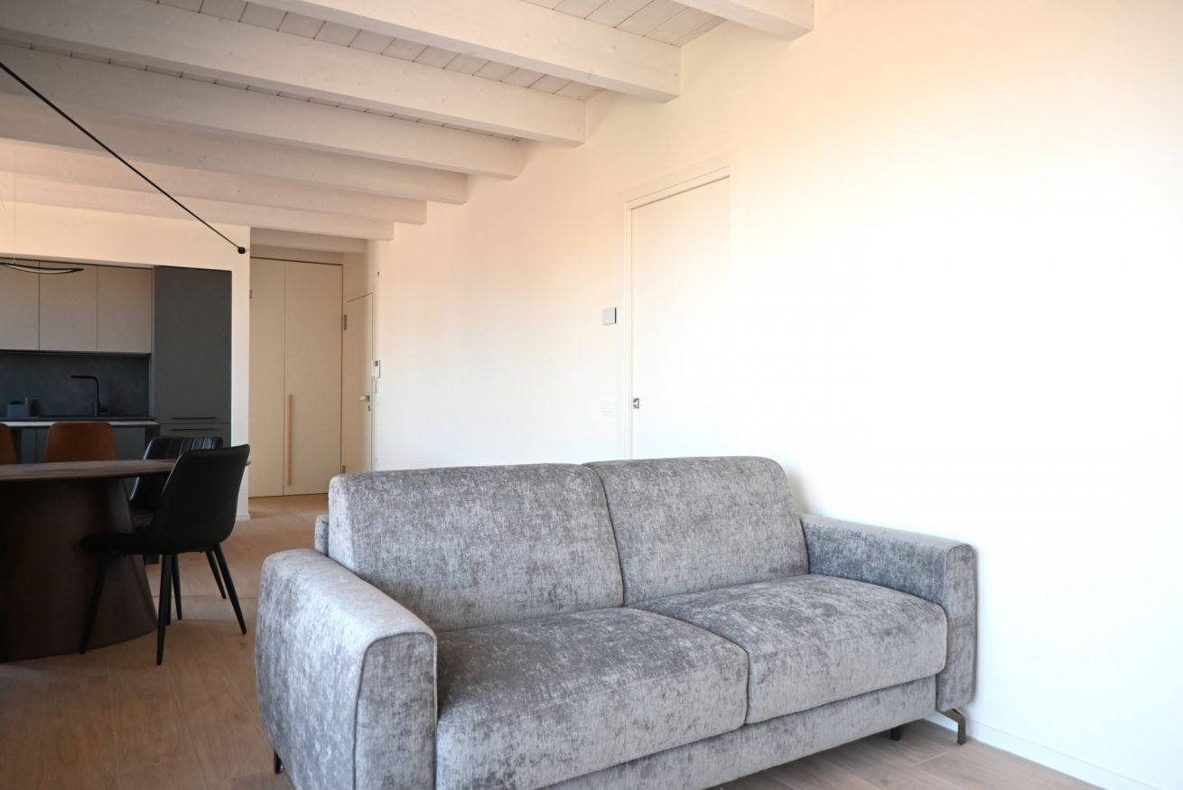 Een moderne woonkamer met een grijze bank, een eethoek met een tafel en stoelen, en een keuken op de achtergrond.