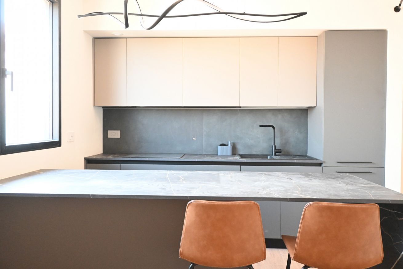 A modern kitchen with a marble countertop, two brown chairs, and a grey backsplash.