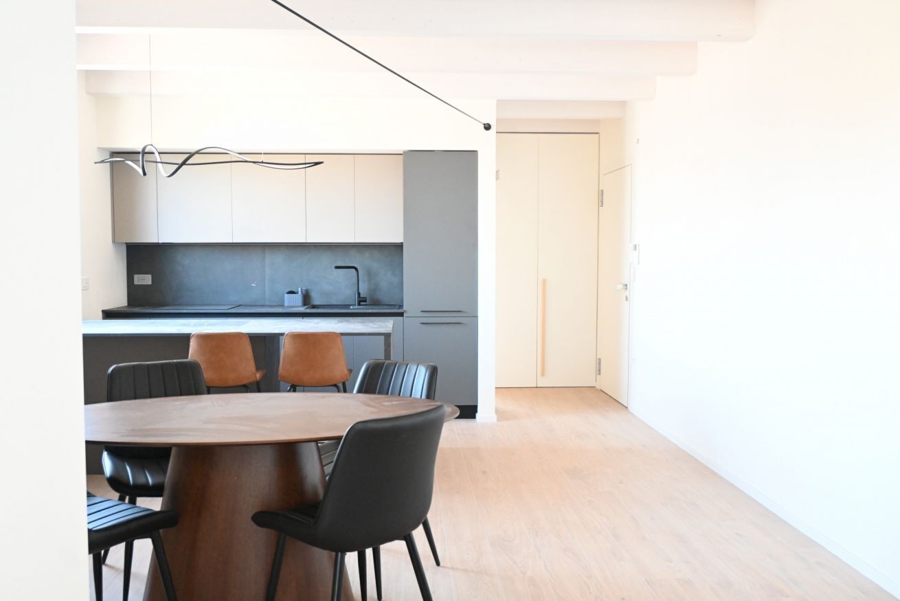 Una cocina moderna con comedor, que incluye una mesa y sillas de madera, una encimera gris y una puerta blanca.