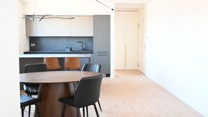 Uma cozinha moderna com área de refeições, com mesa e cadeiras de madeira, bancada cinza e porta branca.
