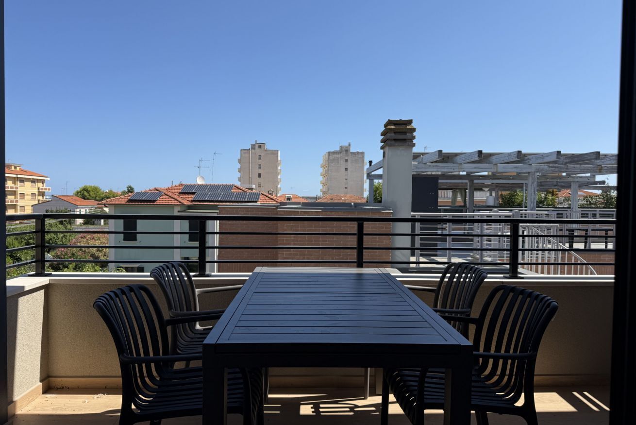 Un balcón con mesa y sillas, que da a una vista de la ciudad con edificios y cielo despejado.