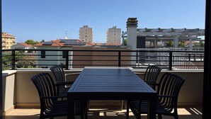 Uma varanda com mesa e cadeiras, com vista para um horizonte urbano repleto de edifícios e céu limpo.