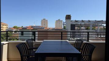 Un balcón con mesa y sillas, que da a una vista de la ciudad con edificios y cielo despejado.