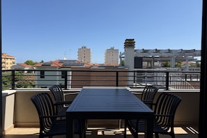Ein Balkon mit Tisch und Stühlen, der auf einen Stadtblick mit Gebäuden und hellem Himmel blickt.